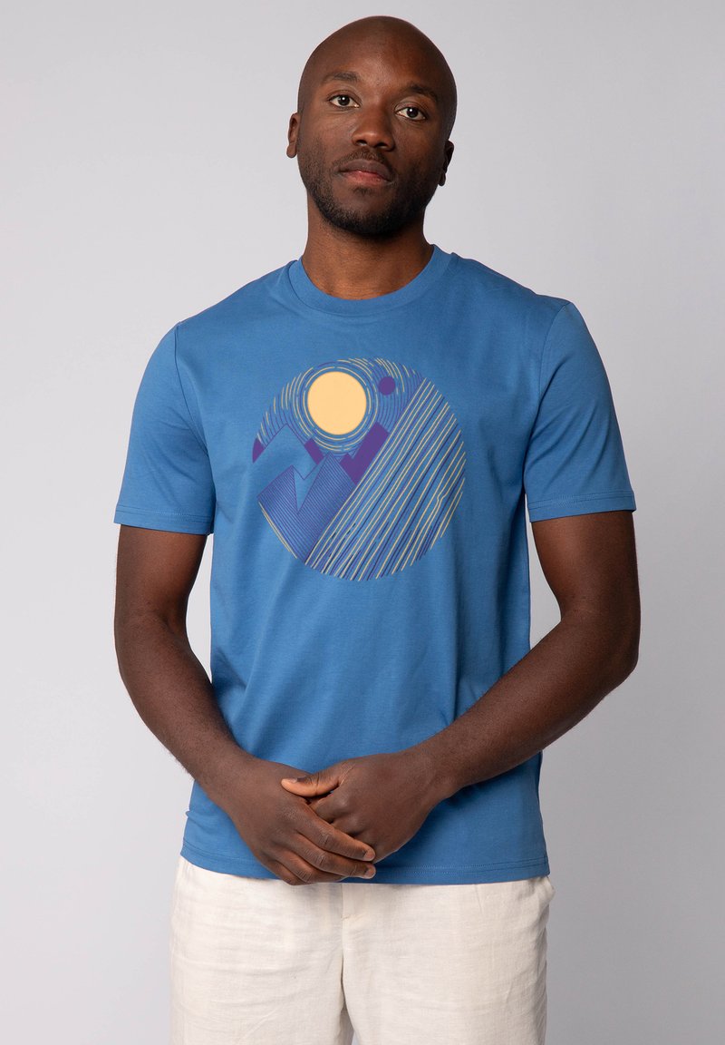 Blauwe katoenen T-shirt met een circulaire graphic van de zon, bergen en lijnen in geel en paars. Korte mouwen en een ronde halslijn.