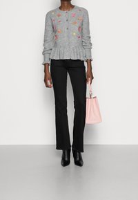 Szary dziergany kardigan z kwiatową haftem, dół z baskinką, czarne rozszerzane dżinsy, czarne szpiczaste botki do kostki oraz mała różowa torebka.