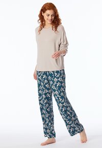 Jasno beżowa bluzka z długim rękawem w połączeniu z ciemno zielonymi spodniami od piżamy z białym wzorem roślinnym, luźny krój i miękka tekstura.