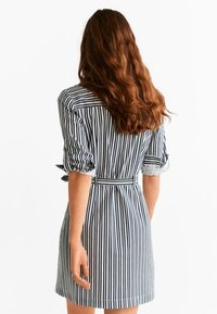 Abito a righe corte in tessuto blu navy e bianco. Presenta una vita con cintura, maniche corte arrotolate e una silhouette aderente.