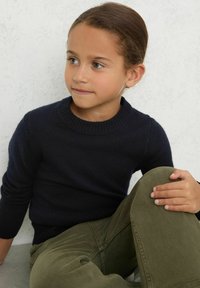 Maglione a maglia blu navy con collo a girocollo a coste, dotato di maniche lunghe. Abbinato a pantaloni verde oliva, caratterizzati da una vestibilità comoda e una texture interessante.