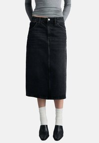 Sort denim midi-nederdel med frontlommer, klassisk design og lige snit. Parres med hvide sokker og sorte sko.