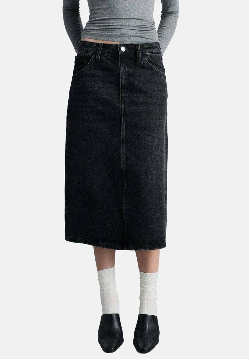 Sort denim midi-nederdel med frontlommer, klassisk design og lige snit. Parres med hvide sokker og sorte sko.