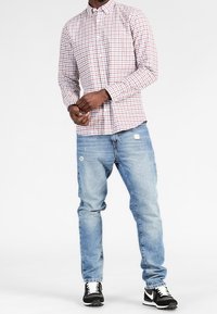 Röd och vit rutmönstrad skjorta med knappar och lång ärm, i kombination med blå slitna jeans och svarta sportskor.