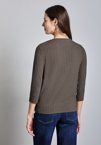 Gestreiftes olivgrünes Oberteil mit drei Viertelärmeln, Bootsausschnitt und gerader Passform, kombiniert mit dunkelblauen Jeans.