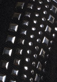 Mustaa kangasta, jossa on kiiltäviä metallisia niittejä eri kokoisina ja muotoisina, mukaan lukien neliö- ja pyöreät, aseteltuna toistuvaan kuvioon.
