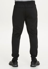 Svarta sweatpants med dragsko i midjan, avsmalnande ben och cuffs vid anklarna. Tillverkade av ett slätt, lätt material.