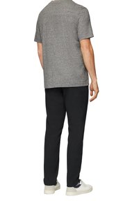 Chemise grise à manches courtes et pantalon noir, fabriqués en tissu doux. Les chaussures sont blanches avec des accents sombres. Design simple et ample.