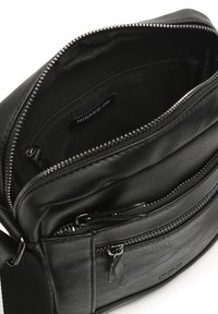 Borsa in pelle nera con compartimento principale con zip e una tasca frontale aggiuntiva. Presenta una texture liscia e dettagli hardware in tono argento.