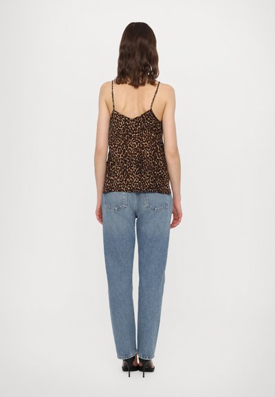 Luipaardprint cami-top met dunne spaghettibandjes, gecombineerd met losse lichtblauwe jeans en zwarte hoge hakken. Eenvoudige achtergrond.