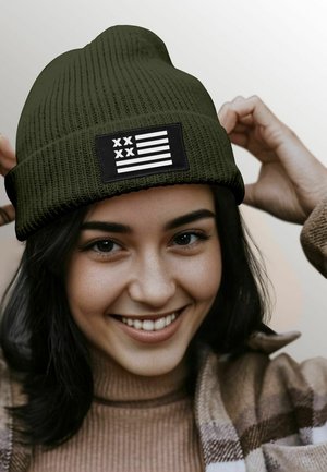 Olive green knit beanie with a black patch featuring white stripes and symbols. Soft texture, fitted shape, suitable for casual wear.