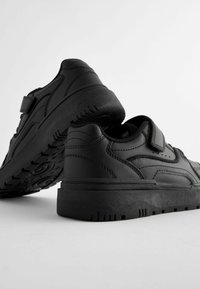 Chaussures de sport noires avec un extérieur en cuir lisse, un col rembourré et une bande Velcro. Semelle en caoutchouc épaisse et à motif pour une bonne adhérence et durabilité.