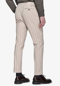 Jasno beżowe spodnie w paski o slim fit, z elastycznym pasem i tylną kieszenią. Zestawione z ciemnymi eleganckimi butami i podwiniętymi mankietami.