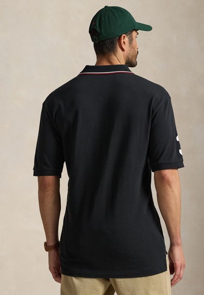 Svart poloshirt med teksturert stoff, med krage og korte ermer. Merkbare røde detaljer på kragen og stor hvit logo på ermet.