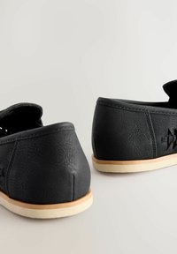 Chaussures en cuir noir avec une finition texturée et une forme arrondie. Présentant une semelle de couleur claire et peu de détails sur les côtés.