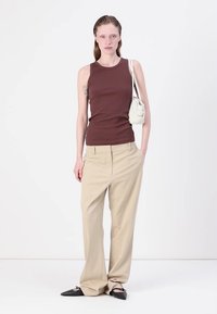 Brun ribbet tanktop, beige vide benbukser, sorte spidse flade sko og en hvid skuldertaske. Modellen står foran en ensfarvet hvid baggrund.