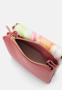 Petit porte-monnaie en cuir rose avec une fermeture éclair dorée ouverte et un rabat en tissu coloré avec des motifs abstraits verts, roses et orange.