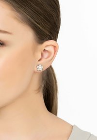 Flower-shaped stud earrings with a central pearl, surrounded by small clear stones, set in silver-tone metal.