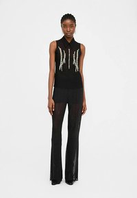 Black sleeveless top with pearl embellishments, paired with black sheer flared pants featuring a subtle sparkle. Both are fitted and lightweight.