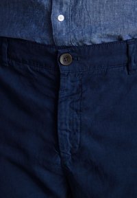 Bermuda blu navy realizzati in tessuto leggero con chiusura a bottone in vita e tasche laterali; texture liscia con un sottile lucido.