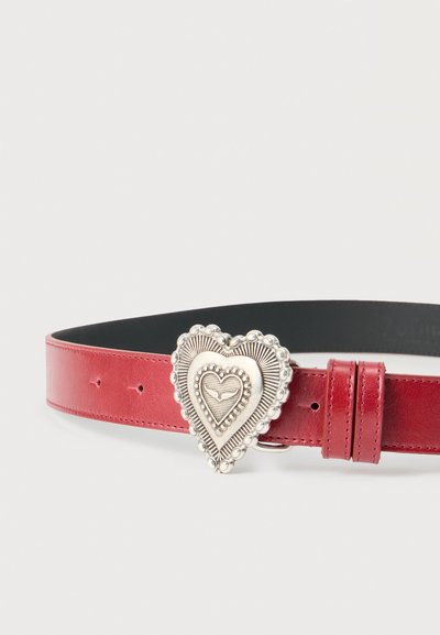 Ζώνη από κόκκινο δέρμα με μεγάλη περίτεχνη καρδιά από ασήμι στο μεταλλικό κούμπωμα, που έχει ακτινωτές γραμμές και μικρές διακοσμητικές χάντρες.