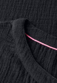 Svart texturerad tyg med rundad nacke, med en rosa accent längs den inre kanten. Materialet verkar mjukt och något rynkat.