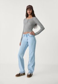 Gray ribbed knit cropped top, light blue straight-leg jeans, brown suede sneakers with white accents, and a brown cap.