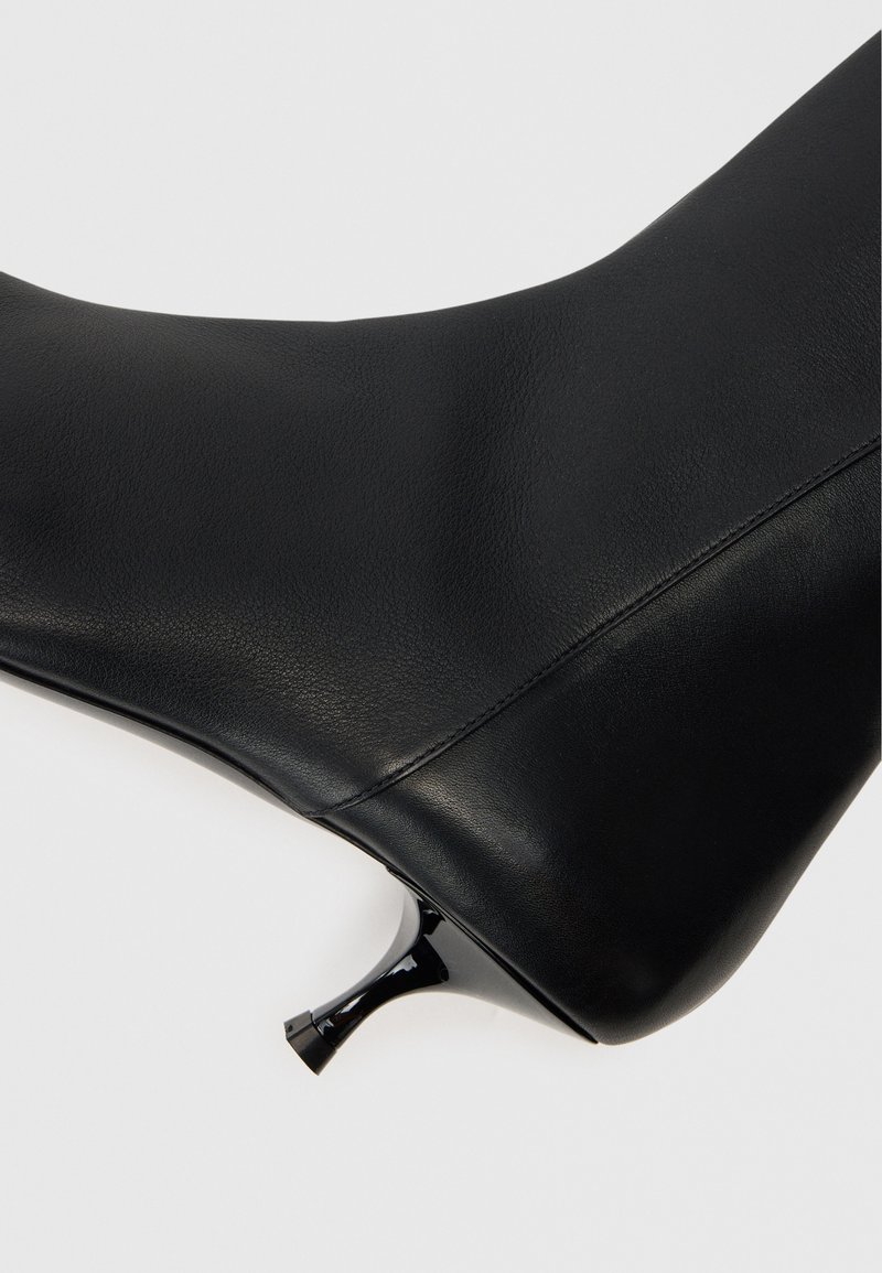Svart läderankelboot med en slank design, spetsig tå och en glänsande, smal klack. Slät textur med synlig sömdetalj.