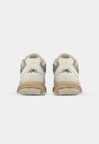 Pair of beige and gray New Balance athletic shoes viewed from the back, showing perforated suede and cushioned soles.