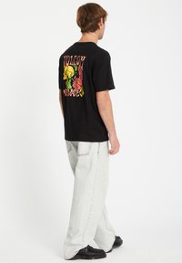 Sort T-shirt med et farverigt kranium og blomster grafik på ryggen. Sammen med lysegrå, løstsiddende jeans og sorte sko.