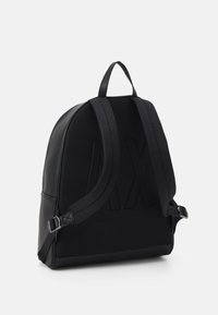 Zaino nero con retro in rete testurizzata, dettagli in pelle liscia, spallacci regolabili e un motivo logo discreto sulla parte anteriore.