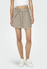 Beiger Wickelrock mit Gürtel, aus Baumwollstoff gefertigt. Verfügt über eine glatte Textur und einen geraden Schnitt, kombiniert mit weißen Turnschuhen.