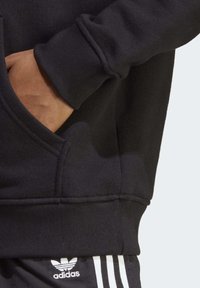 Svart sweatshirt med mjuk textur, som har en känguruficka, ribbade mudd och nederkant; kombinerad med svarta och vita randiga byxor.