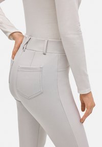 Pantalones de talle alto en gris claro con una textura suave, que cuentan con dos bolsillos traseros y detalles de costura sutiles. Vista en primer plano desde atrás.
