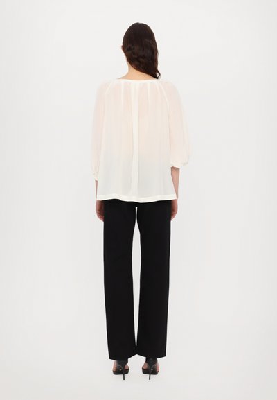 Blouse blanche ample et légère avec un col rond et des manches bouffantes, assortie à un pantalon noir taille haute et des talons. Design simple et élégant.