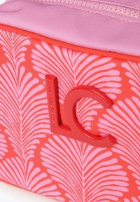 Neceser de cosméticos con un diseño de colores rojos y acentos en rosa, que presenta una etiqueta de logo rojo en relieve y un cierre de cremallera suave. Diseño floral en la tela.