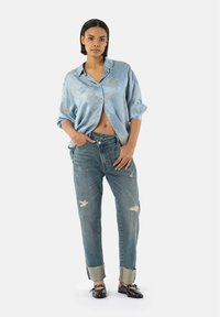 Light blue satin button-up shirt with floral pattern, worn with distressed light wash jeans rolled at the cuffs. Black slip-on shoes.