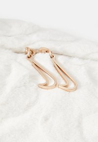 Gullfargede metallørsene med buet design, som hviler på en myk, hvit pelsbakgrunn, med glatte og polerte overflater.