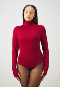 Červený body s dlhým rukávom a vysokým golierom, vyrobený z hladkej tkaniny. Nosený s čiernymi priesvitnými pančuchami s bodkami, ktoré predvádzajú priliehavý strih.
