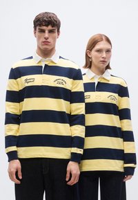 Ριγωτά ριμπ σώματος από βαμβάκι σε κίτρινο και ναυτικό μπλε, με λευκό γιακά, κεντημένα λογότυπα και μακριά μανίκια.