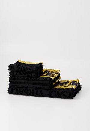 Črne brisače zložene, s zlatimi vzorci in potezami. Brisače prikazujejo teksturirano blago z vidnim logotipom Versace.