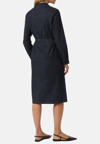 Czarna sukienka koszulowa z denimu, z paskiem w talii, długimi rękawami i długością do kolan. Posiada kontrastowe przeszycia i klasyczny kołnierzyk.