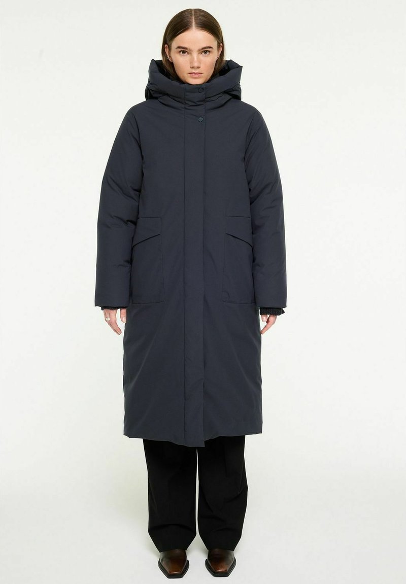 Lång mörk marinblå puffjacka med hög krage, huva och två fickor fram. Har en knappstängning och en slät, mjuk textur.