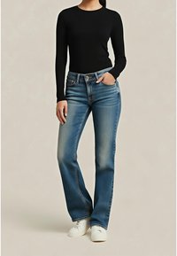 Haut noir à manches longues associé à un jean bleu clair à jambes droites, présentant une texture délavée. Modèle portant des baskets blanches.