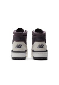 Vysoké tenisky s šedým a černým semišovým povrchem, polstrovaným límcem a texturovanou gumovou podrážkou; obsahují logo New Balance v černé barvě.