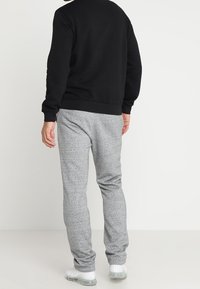 Felpa nera e pantaloni jogging grigi, realizzati in materiale morbido. I pantaloni jogging hanno una vita elasticizzata e una finitura testurizzata, con una vestibilità slim.