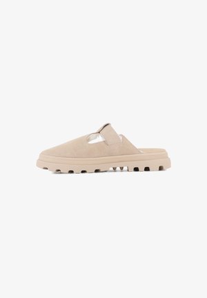 Chaussure slip-on en suède beige avec un design découpé, une semelle texturée et un coussin à l'intérieur. Elle dispose d'une sangle pour un maintien sécurisé.