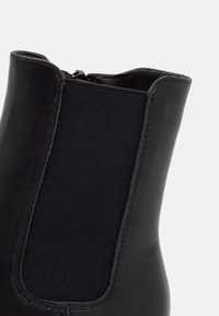 Černé kožené kotníkové boty s elastickým bočním panelem, hladkým texturem a zipovým zapínáním vzadu pro snadné obouvání.