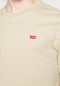 Beige T-Shirt mit kurzen Ärmeln aus Baumwolle, mit rundem Ausschnitt und einem kleinen roten Levi's Logo-Label auf der linken Brust.