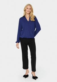 Maglietta viola a maniche lunghe con scollo a V, abbinata a pantaloni neri a gamba dritta e scarpe nere slip-on con dettagli a fiocco.